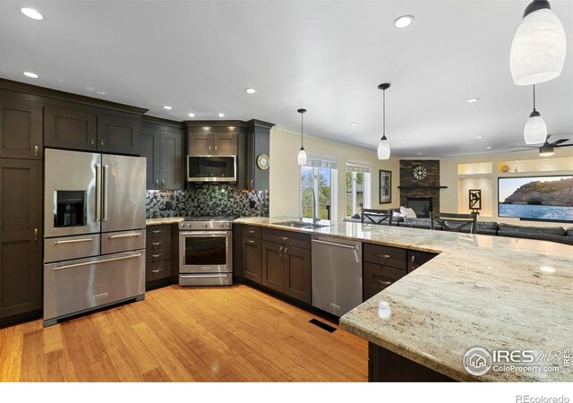 1119 Wrangler Way, Loveland, CO 80537 - kitchen featuring appliances with stainless steel finishes, a large fireplace, a sink, light wood-type flooring, and tasteful backsplash