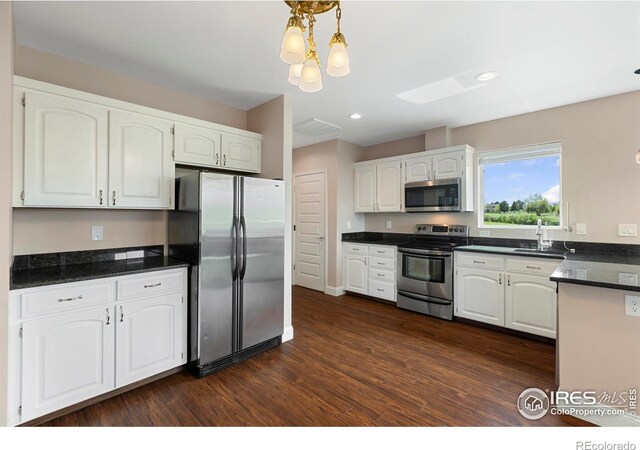 1119 Wrangler Way, Loveland, CO 80537 - kitchen with appliances with stainless steel finishes, white cabinetry, dark countertops, dark wood-type flooring, and decorative light fixtures