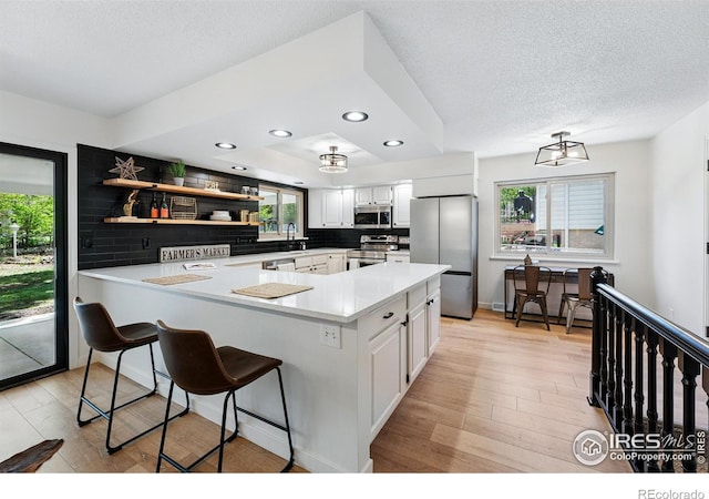 1832 24th Avenue Pl, Greeley, CO 80634 - kitchen featuring appliances with stainless steel finishes, light wood finished floors, plenty of natural light, white cabinetry, and a textured ceiling