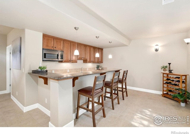 8245 Hidden Cove Ct, Windsor, CO 80528 - kitchen featuring stainless steel microwave, a kitchen bar, brown cabinets, and light tile patterned floors