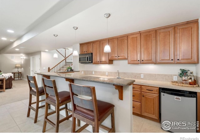 8245 Hidden Cove Ct, Windsor, CO 80528 - kitchen featuring appliances with stainless steel finishes, a kitchen bar, light tile patterned floors, brown cabinets, and recessed lighting