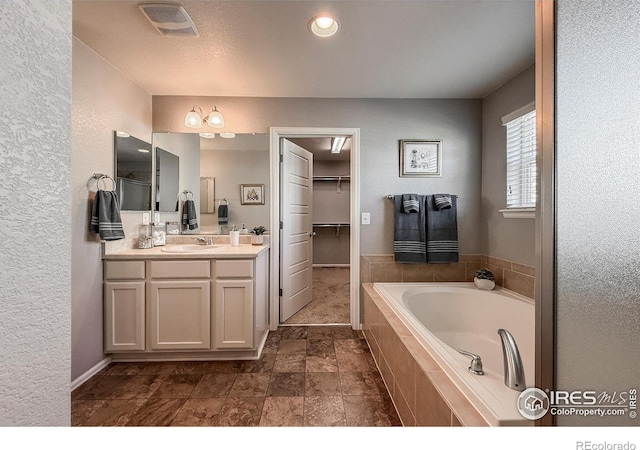 2190 Winding Dr, Longmont, CO 80504 - bathroom with double vanity, a bath, a spacious closet, and a textured wall