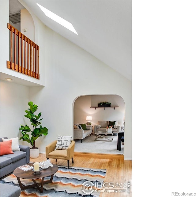 911 Homer Cir, Lafayette, CO 80026 - living area with arched walkways, a skylight, high vaulted ceiling, wood finished floors, and baseboards
