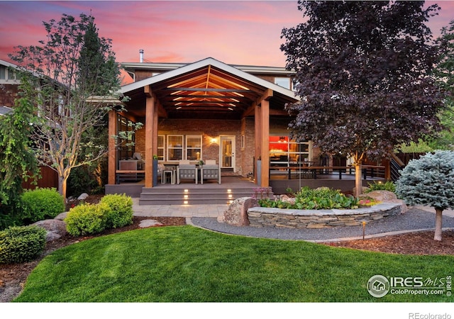 317 Wood St, Fort Collins, CO 80521 - back of house at dusk with a yard, an outdoor hangout area, a deck, and brick siding