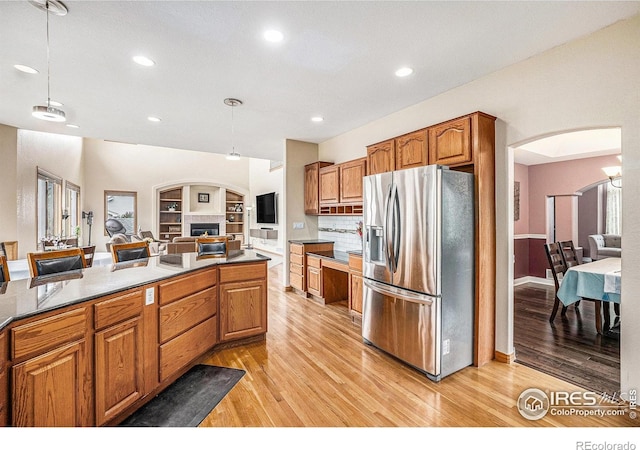 13971 Telluride Dr, Broomfield, CO 80020 - kitchen featuring stainless steel fridge with ice dispenser, light wood-style flooring, brown cabinets, arched walkways, and recessed lighting