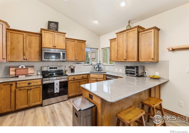 6848 Pettigrew St, Wellington, CO 80549 - kitchen with appliances with stainless steel finishes, vaulted ceiling, brown cabinetry, a kitchen breakfast bar, and decorative backsplash