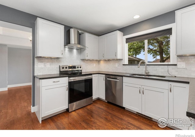 531 S 9th St, Berthoud, CO 80513 - kitchen with wall chimney range hood, appliances with stainless steel finishes, a sink, dark countertops, and dark wood-type flooring