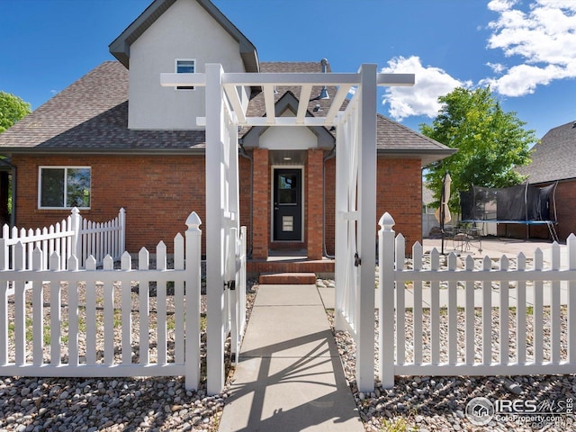 101 SE 2nd St, Berthoud, CO 80513 - view of front facade with brick siding, a trampoline, a shingled roof, and a fenced front yard