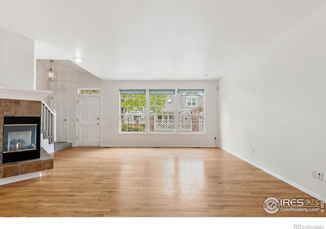 2982 W Long Dr # C, Littleton, CO 80120 - unfurnished living room featuring light wood-style flooring, baseboards, lofted ceiling, and a tile fireplace