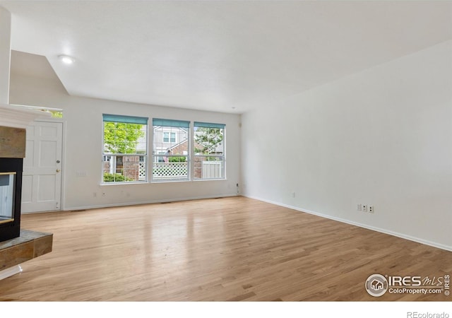 2982 W Long Dr # C, Littleton, CO 80120 - unfurnished living room with light wood-type flooring, a tiled fireplace, baseboards, and lofted ceiling