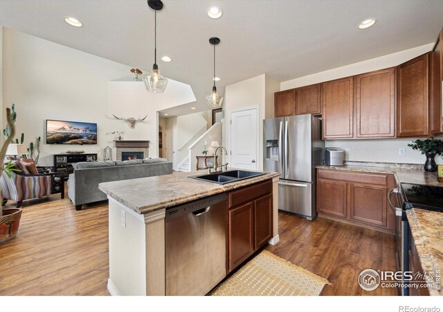 7401 Pimlico Dr, Windsor, CO 80550 - kitchen featuring appliances with stainless steel finishes, a sink, wood finished floors, decorative light fixtures, and a lit fireplace