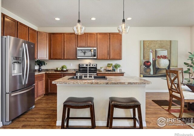 7401 Pimlico Dr, Windsor, CO 80550 - kitchen featuring appliances with stainless steel finishes, a sink, dark wood finished floors, recessed lighting, and a breakfast bar