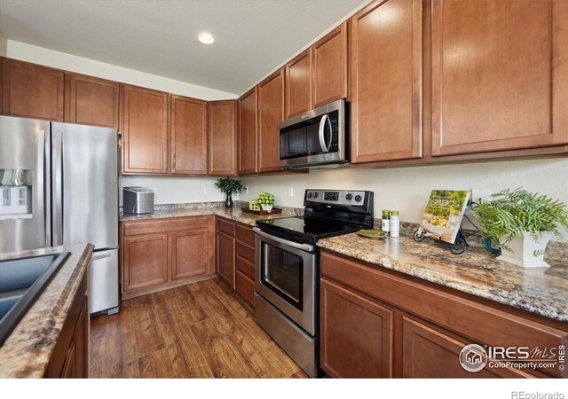 7401 Pimlico Dr, Windsor, CO 80550 - kitchen with appliances with stainless steel finishes, dark wood finished floors, brown cabinets, a sink, and recessed lighting