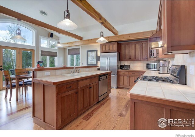 9445 Lykins Pl, Boulder, CO 80301 - kitchen with a sink, appliances with stainless steel finishes, tile counters, decorative backsplash, and light wood-style flooring