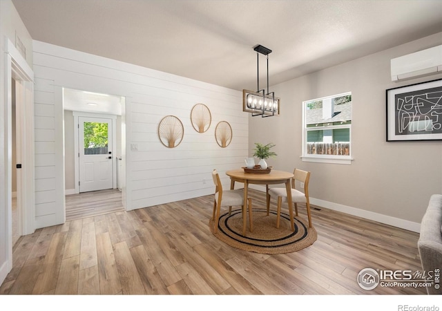 217 Locust St, Windsor, CO 80550 - dining space with an AC wall unit, light wood-type flooring, wood walls, a chandelier, and baseboards