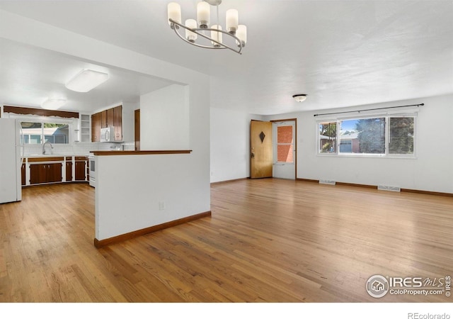1229 Juniper St, Longmont, CO 80501 - unfurnished living room featuring a chandelier, healthy amount of natural light, light wood-style flooring, and baseboards