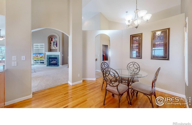 8211 Lighthouse Lane Ct, Windsor, CO 80528 - dining space featuring arched walkways, light wood-style floors, a chandelier, baseboards, and a fireplace