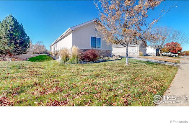 8211 Lighthouse Lane Ct, Windsor, CO 80528 - view of home's exterior featuring stone siding, driveway, stucco siding, an attached garage, and a lawn