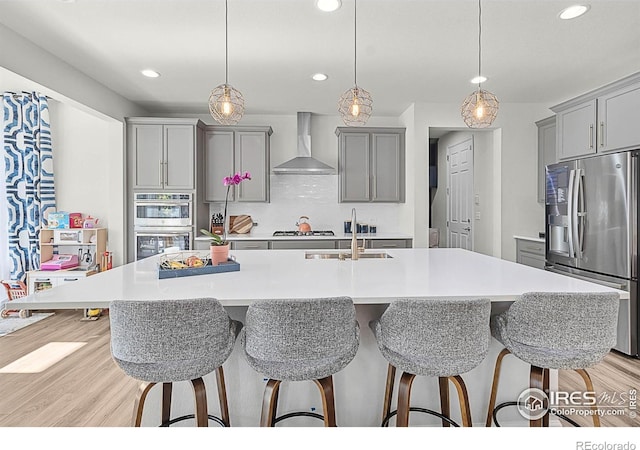 6229 Black Mesa Rd, Frederick, CO 80516 - kitchen with stainless steel appliances, wall chimney exhaust hood, gray cabinetry, a sink, and a kitchen bar