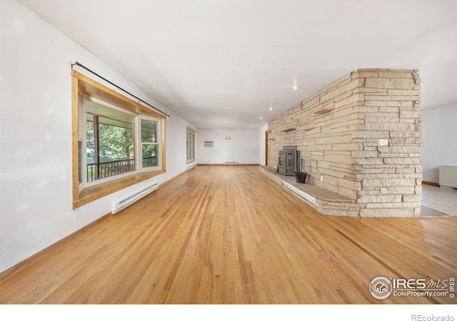 23462 County Road 55, Kersey, CO 80644 - unfurnished living room with a baseboard heating unit, light wood finished floors, a wood stove, a baseboard radiator, and baseboards