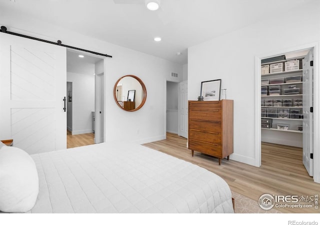 12155 W 57th Pl, Arvada, CO 80002 - bedroom with a barn door, a walk in closet, light wood-type flooring, recessed lighting, and a closet