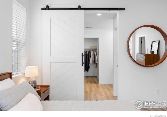 12155 W 57th Pl, Arvada, CO 80002 - bedroom featuring a barn door, a spacious closet, wood finished floors, and multiple windows