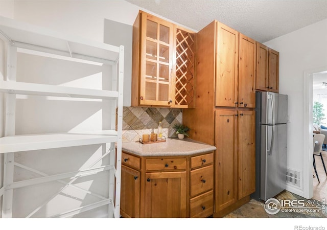 135 E 8th Ave, Denver, CO 80203 - kitchen with freestanding refrigerator, decorative backsplash, glass insert cabinets, light countertops, and brown cabinetry