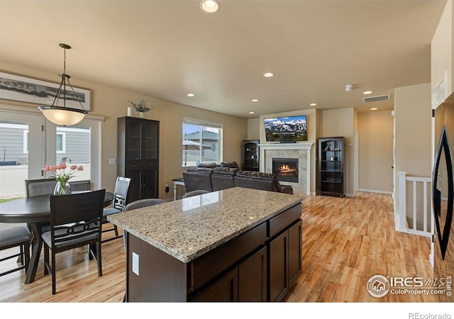 3802 Eucalyptus St, Wellington, CO 80549 - kitchen featuring light wood-type flooring, a tile fireplace, dark brown cabinetry, hanging light fixtures, and a kitchen island