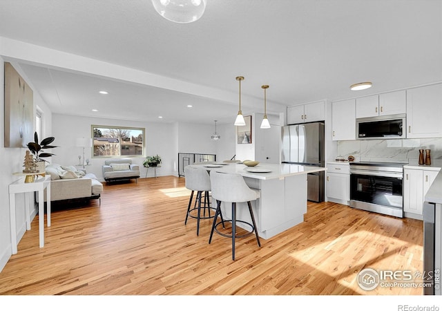4642 Everett Ct, Wheat Ridge, CO 80033 - kitchen featuring appliances with stainless steel finishes, light wood finished floors, white cabinets, open floor plan, and backsplash