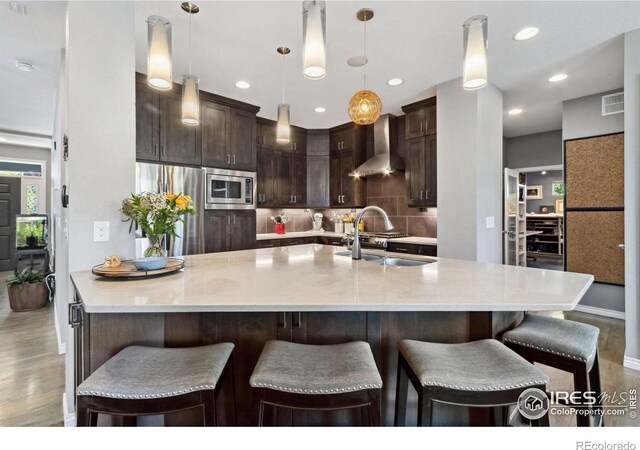 2620 Brush Creek Dr, Fort Collins, CO 80528 - kitchen featuring wall chimney range hood, stainless steel appliances, dark brown cabinetry, a sink, and backsplash