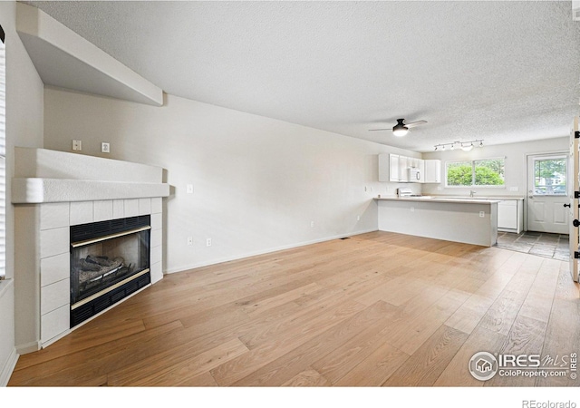 3022 W 107th Pl Unit D, Westminster, CO 80031 - unfurnished living room featuring light wood finished floors, a ceiling fan, a textured ceiling, a fireplace, and baseboards