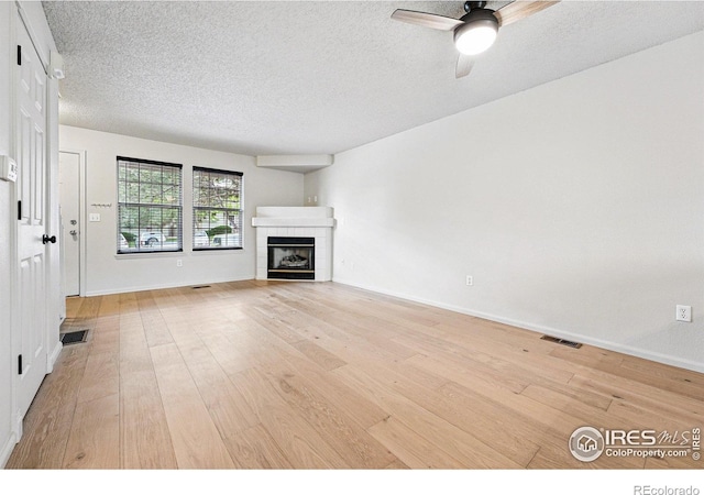 3022 W 107th Pl Unit D, Westminster, CO 80031 - unfurnished living room featuring light wood-style floors, a textured ceiling, a ceiling fan, a tile fireplace, and baseboards