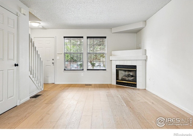 3022 W 107th Pl Unit D, Westminster, CO 80031 - unfurnished living room with light wood-style flooring, a textured ceiling, a tile fireplace, baseboards, and stairs