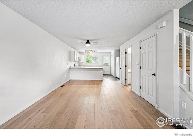 3022 W 107th Pl Unit D, Westminster, CO 80031 - unfurnished living room featuring light wood-style floors, stairway, a textured ceiling, ceiling fan, and baseboards