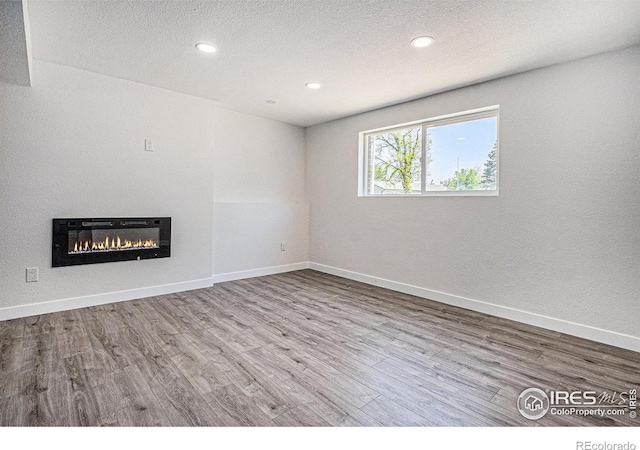15904 E Bates Pl, Aurora, CO 80013 - unfurnished living room with wood finished floors, a glass covered fireplace, recessed lighting, baseboards, and a textured ceiling