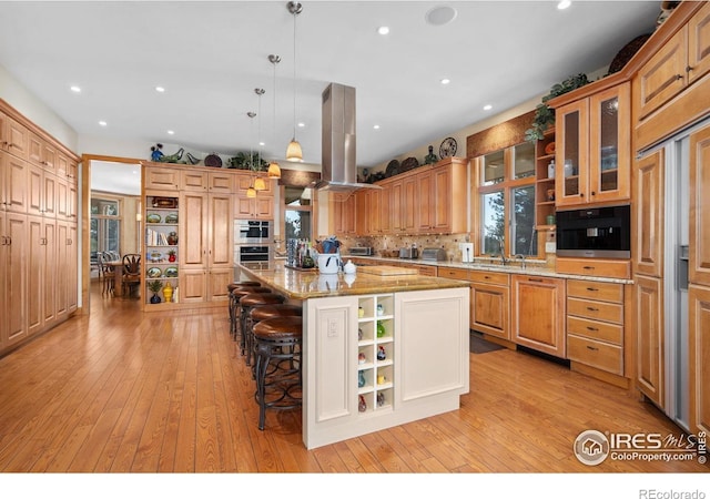 5025 Eagle Lake Dr, Fort Collins, CO 80524 - kitchen with island range hood, a kitchen bar, glass insert cabinets, a spacious island, and light wood-type flooring