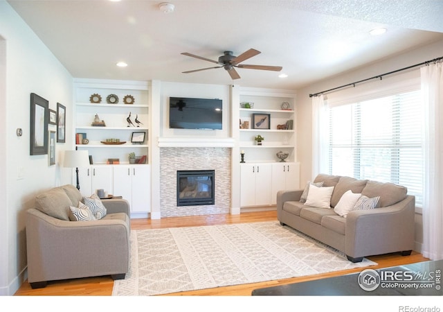 6523 Spanish Bay Dr, Windsor, CO 80550 - living room featuring a ceiling fan, wood finished floors, a glass covered fireplace, built in features, and recessed lighting