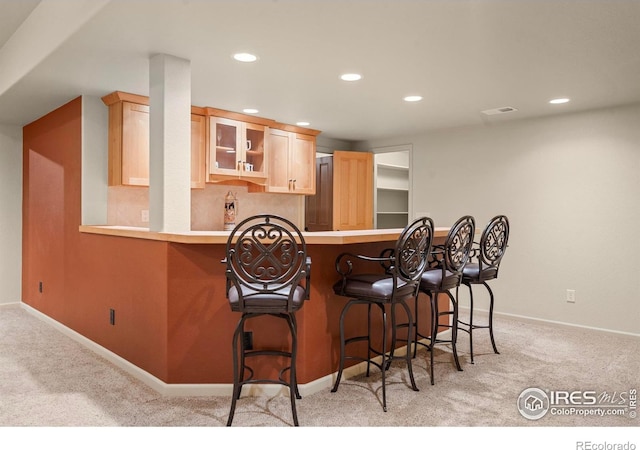 6535 Half Moon Bay Dr, Windsor, CO 80550 - kitchen featuring light colored carpet, light brown cabinets, glass insert cabinets, recessed lighting, and a breakfast bar area