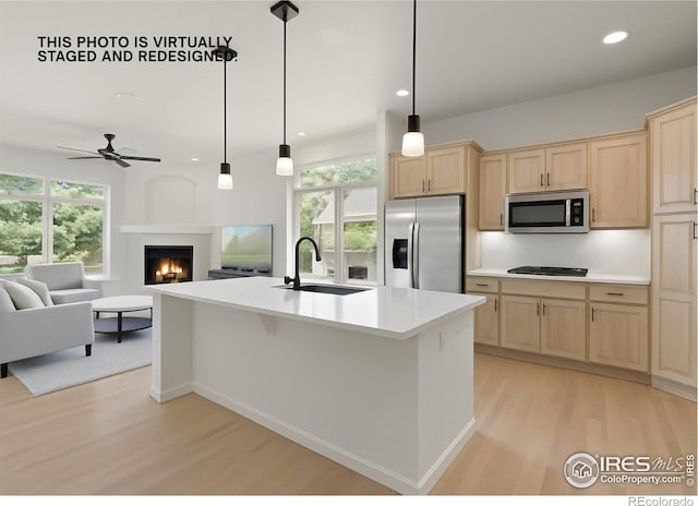 6535 Half Moon Bay Dr, Windsor, CO 80550 - kitchen with appliances with stainless steel finishes, light brown cabinetry, light wood finished floors, light countertops, and a lit fireplace