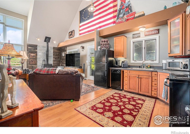 3412 Erving Ct, Berthoud, CO 80513 - kitchen with black appliances, a sink, high vaulted ceiling, a wood stove, and light wood-style flooring