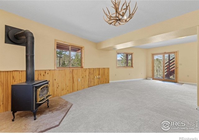 880 Hummer Dr, Nederland, CO 80466 - unfurnished living room with a wainscoted wall, a wood stove, plenty of natural light, carpet flooring, and wooden walls