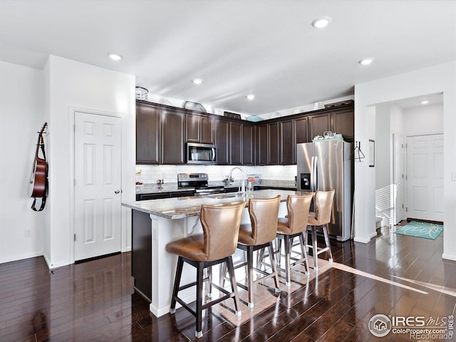 17616 Bluetrail Ave, Parker, CO 80134 - kitchen with stainless steel appliances, dark wood finished floors, dark brown cabinets, light stone counters, and a kitchen island with sink
