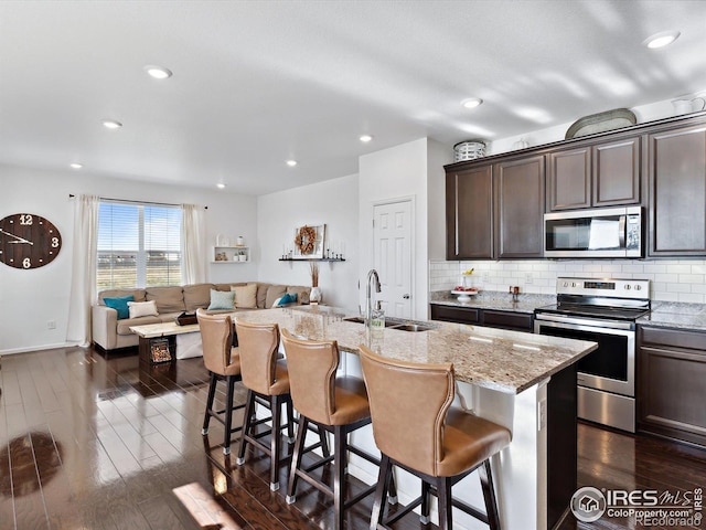 17616 Bluetrail Ave, Parker, CO 80134 - kitchen with appliances with stainless steel finishes, dark brown cabinetry, dark wood-style flooring, a breakfast bar, and recessed lighting