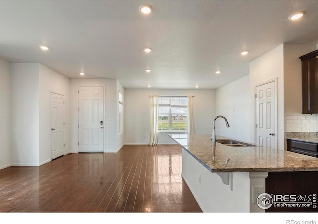 17616 Bluetrail Ave, Parker, CO 80134 - kitchen with light stone countertops, a kitchen island with sink, decorative backsplash, dark wood-style floors, and recessed lighting