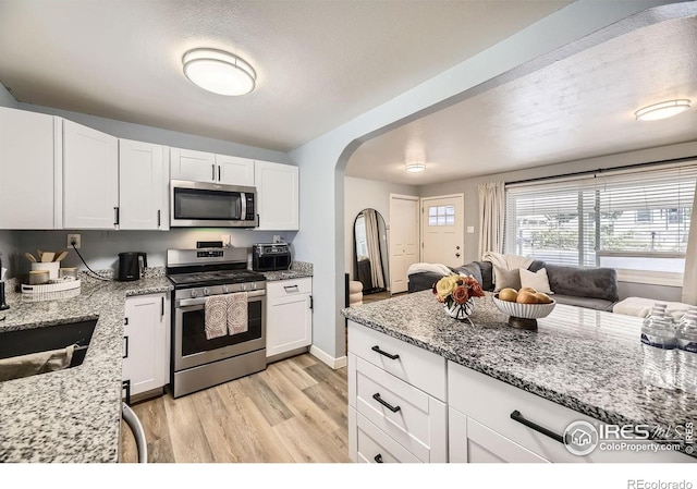 3245 W Walsh Pl, Denver, CO 80219 - kitchen featuring stainless steel appliances, light wood-type flooring, arched walkways, white cabinetry, and light stone counters