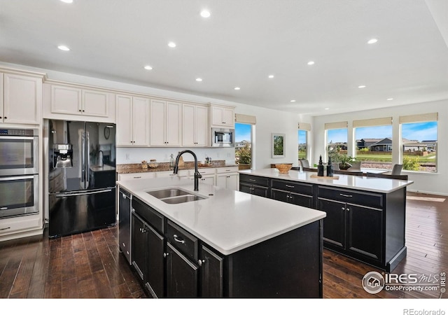 6614 Neota Creek Ct, Timnath, CO 80547 - kitchen with appliances with stainless steel finishes, a kitchen island with sink, a sink, dark cabinetry, and recessed lighting