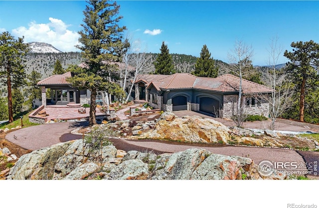 290 Skyhill Dr, Evergreen, CO 80439 - view of front facade with stone siding, a tiled roof, a mountain view, a garage, and asphalt driveway