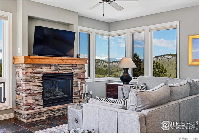 290 Skyhill Dr, Evergreen, CO 80439 - living room featuring ceiling fan, a stone fireplace, dark stone finish floors, and baseboards