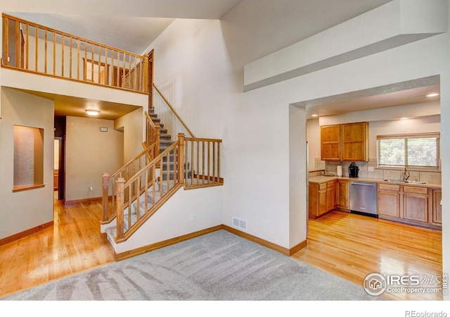 1414 Sheep Creek Ct, Fort Collins, CO 80526 - kitchen featuring stainless steel dishwasher, light wood-type flooring, a sink, baseboards, and a towering ceiling
