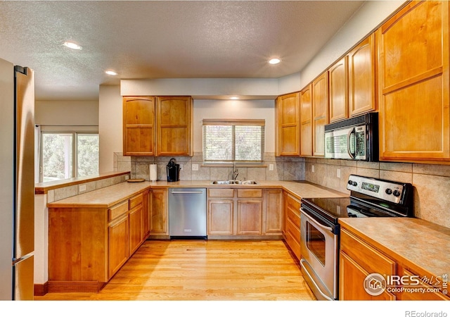 1414 Sheep Creek Ct, Fort Collins, CO 80526 - kitchen featuring appliances with stainless steel finishes, a textured ceiling, light countertops, light wood-style flooring, and a peninsula